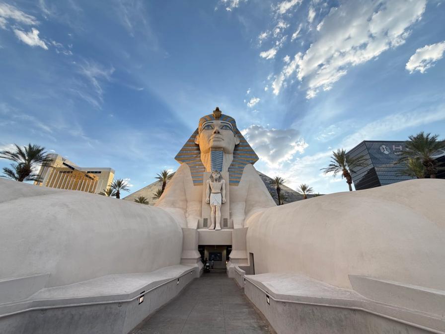 The Great Sphinx replica at the Luxor Hotel in Las Vegas, with a walkway leading between its paws under a bright blue sky.