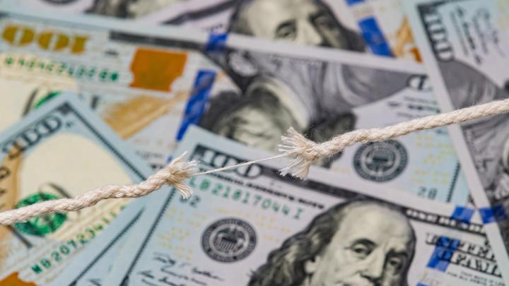 A frayed rope on the verge of snapping, stretched over a background of scattered US hundred-dollar bills.