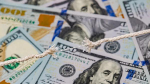 A frayed rope on the verge of snapping, stretched over a background of scattered US hundred-dollar bills.