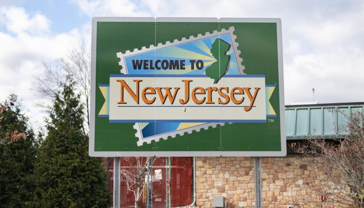 A green road sign reading "Welcome to New Jersey" with a stamp graphic of the state's outline.
