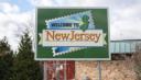 A green road sign reading "Welcome to New Jersey" with a stamp graphic of the state's outline.
