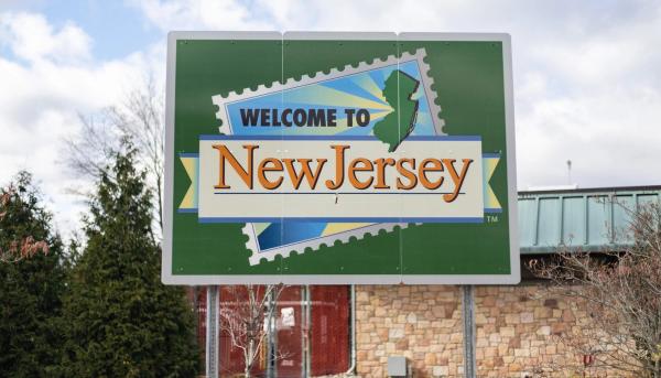 A green road sign reading "Welcome to New Jersey" with a stamp graphic of the state's outline.