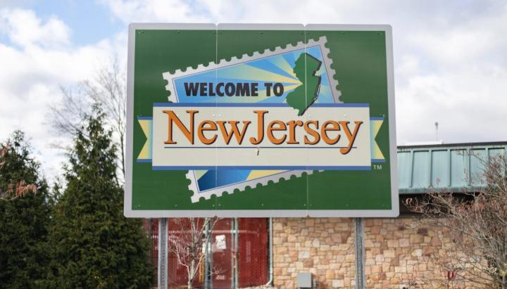 A green road sign reading "Welcome to New Jersey" with a stamp graphic of the state's outline.