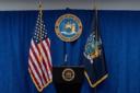 New York Attorney General podium flanked by the US and New York State flags against a blue curtain backdrop.