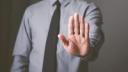 A person in a grey dress shirt and tie holding up an open palm in a stop gesture.