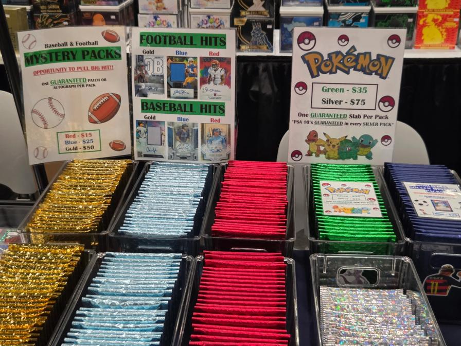 Bins of colorful mystery packs (gold, blue, red, green, silver) at a card show, with signs for sports and Pokémon cards.