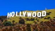 The iconic Hollywood sign on a grassy hill under a clear blue sky.