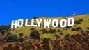The iconic Hollywood sign on a grassy hill under a clear blue sky.