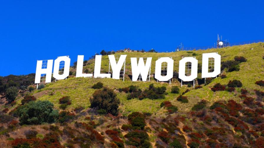 The iconic Hollywood sign on a grassy hill under a clear blue sky.