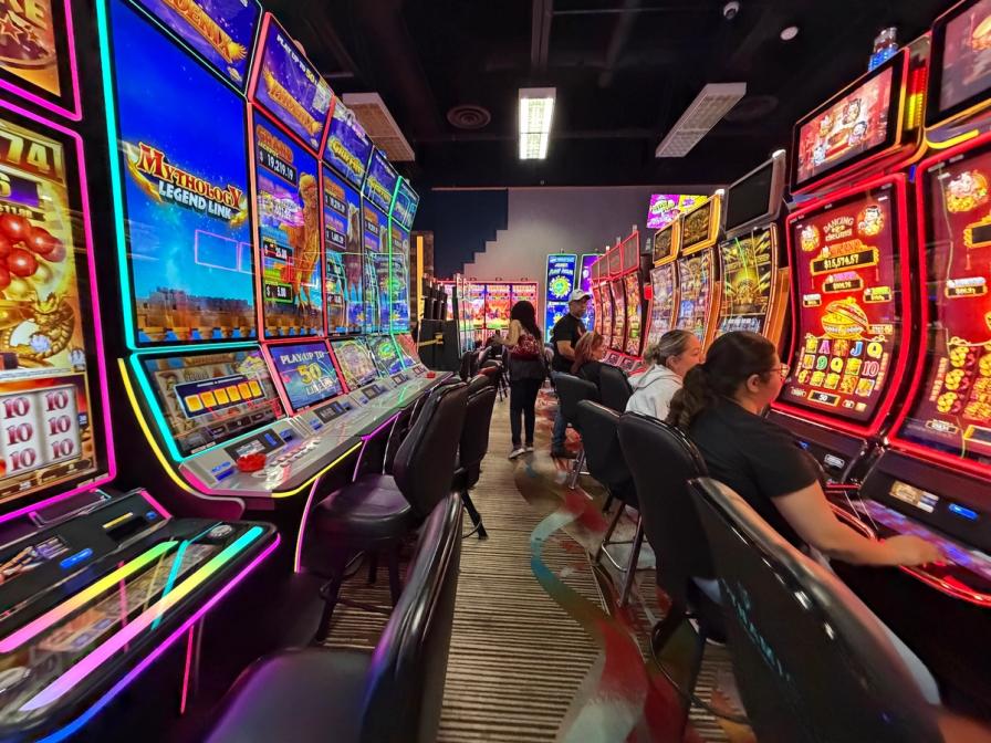 People playing vibrant, brightly lit slot machines in a casino aisle.