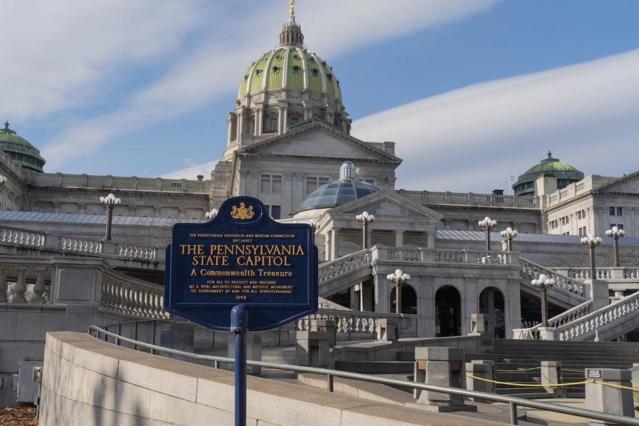 The Pennsylvania State Capitol building with a blue historical marker sign in the foreground.
