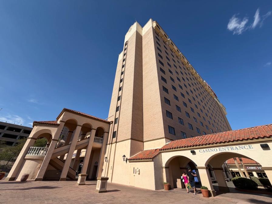Low-angle view of a tall beige casino hotel with a Spanish-style arched entrance under a clear blue sky.
