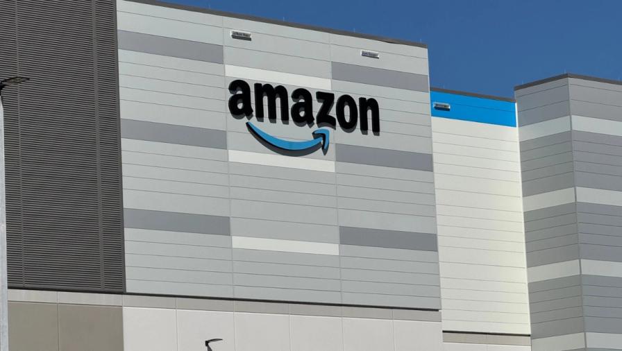 The exterior of a modern Amazon fulfillment center building with the company logo on the facade.