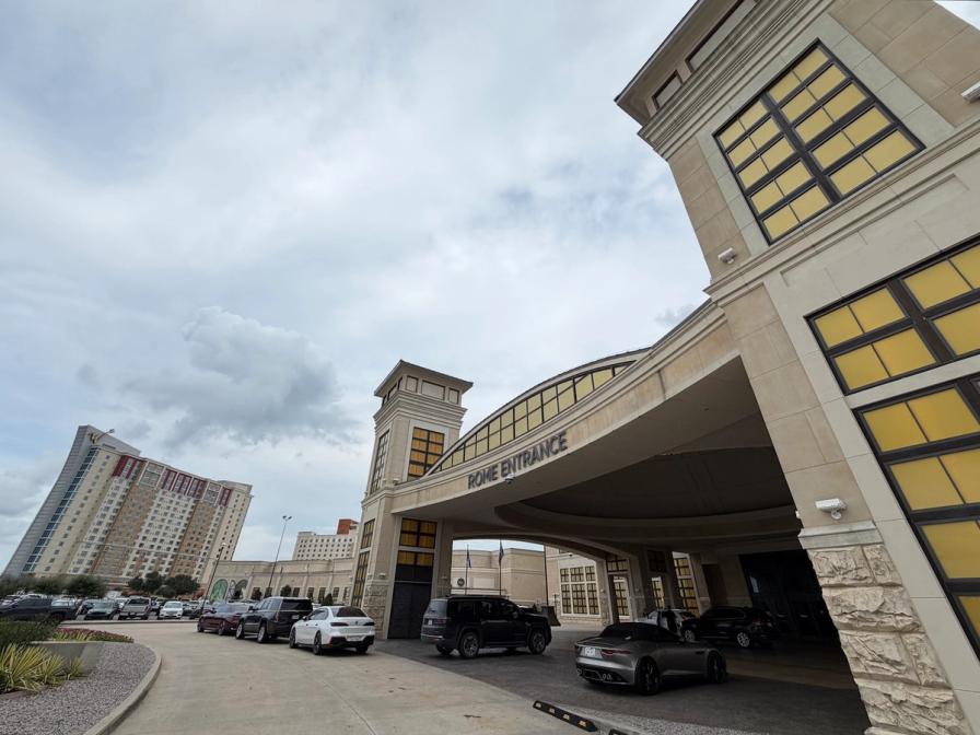 The grand "Rome Entrance" of a building with cars parked under a large canopy and a