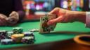 Close-up of a hand holding the King and Queen of Spades over a green poker table with stacks of chips.