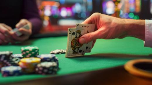 Close-up of a hand holding the King and Queen of Spades over a green poker table with stacks of chips.