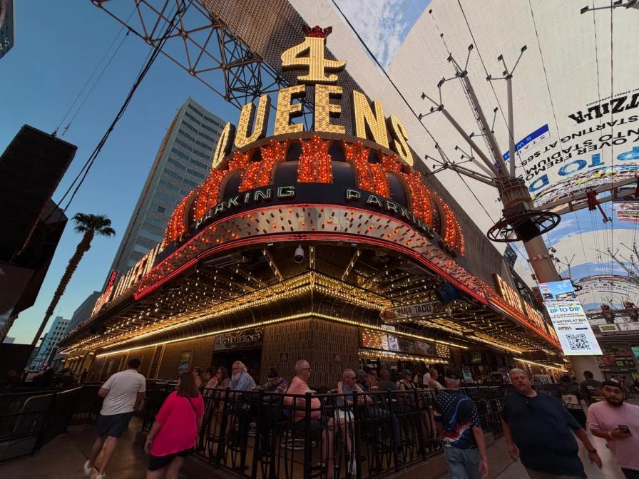 Brightly lit 4 Queens casino sign on Fremont Street in Las Vegas, with pedestrians and an outdoor patio below.