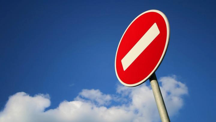 Red "no entry" sign with a white diagonal bar against a blue sky with clouds.