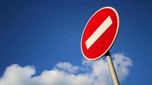 Red "no entry" sign with a white diagonal bar against a blue sky with clouds.
