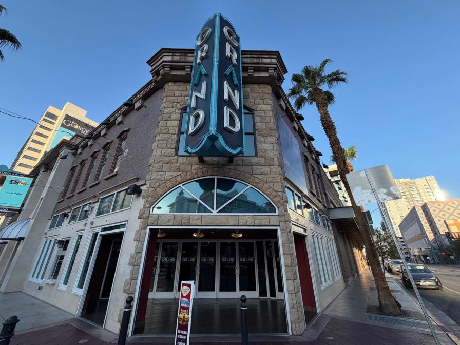 The corner entrance of a stone building with a large vertical neon sign reading "GRAND" next