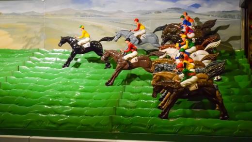 A vintage mechanical horse racing game featuring plastic horses and jockeys on a tiered green track.