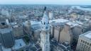 Aerial view of Philadelphia City Hall's white clock tower topped with the William Penn statue, surrounded by the city skyline.