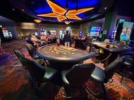 Empty blackjack tables on a casino floor with players and slot machines in the background under a star-shaped ceiling light.