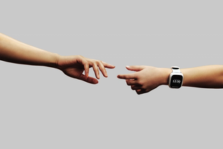 Zwei Hände strecken sich einander entgegen, eine Hand mit einer Spacetalk-Uhr