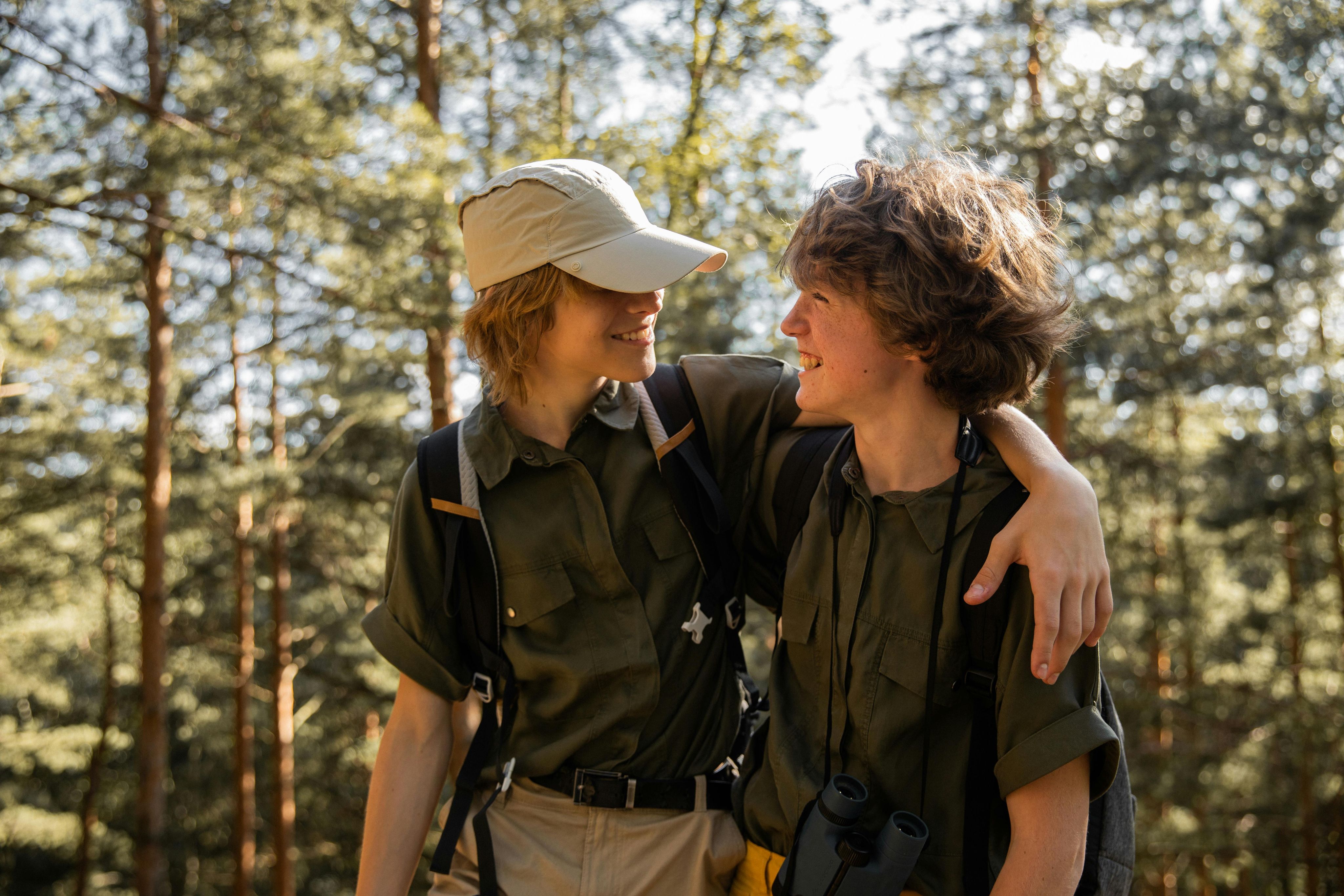 Dos jóvenes excursionistas sonriendo con un brazo alrededor del otro en un bosque.