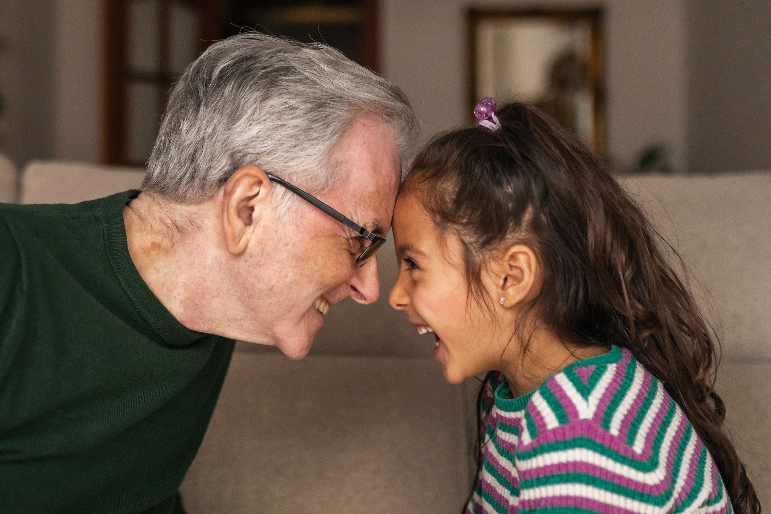 A grandfather smiling heads touching their grandaughter