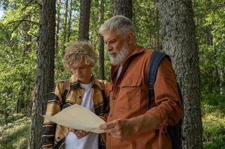 An older man and a young man in a forest look at a map.