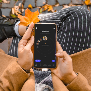 A hand holds a smartphone displaying the SPACETALK app logo surrounded by a circular arrangement of small images.
