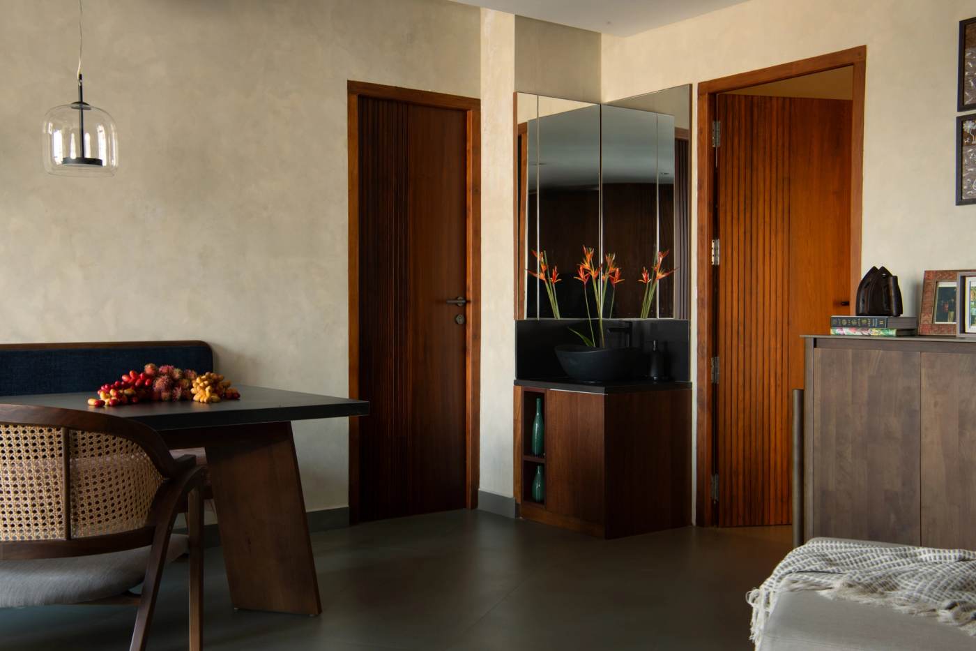 A dining table beside the mirrored washbasin niche, between two timber doors