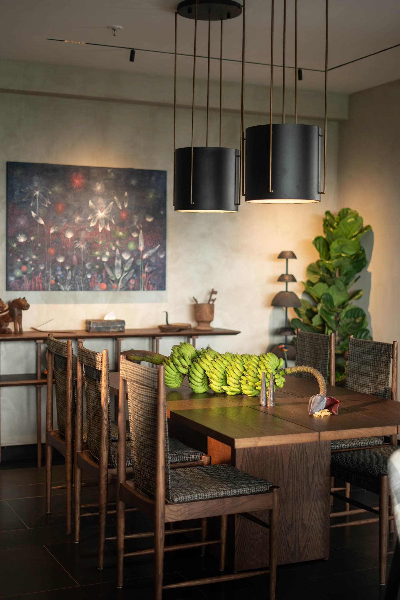 The dining room seen whole, pendants hung low over a table laid with plantains