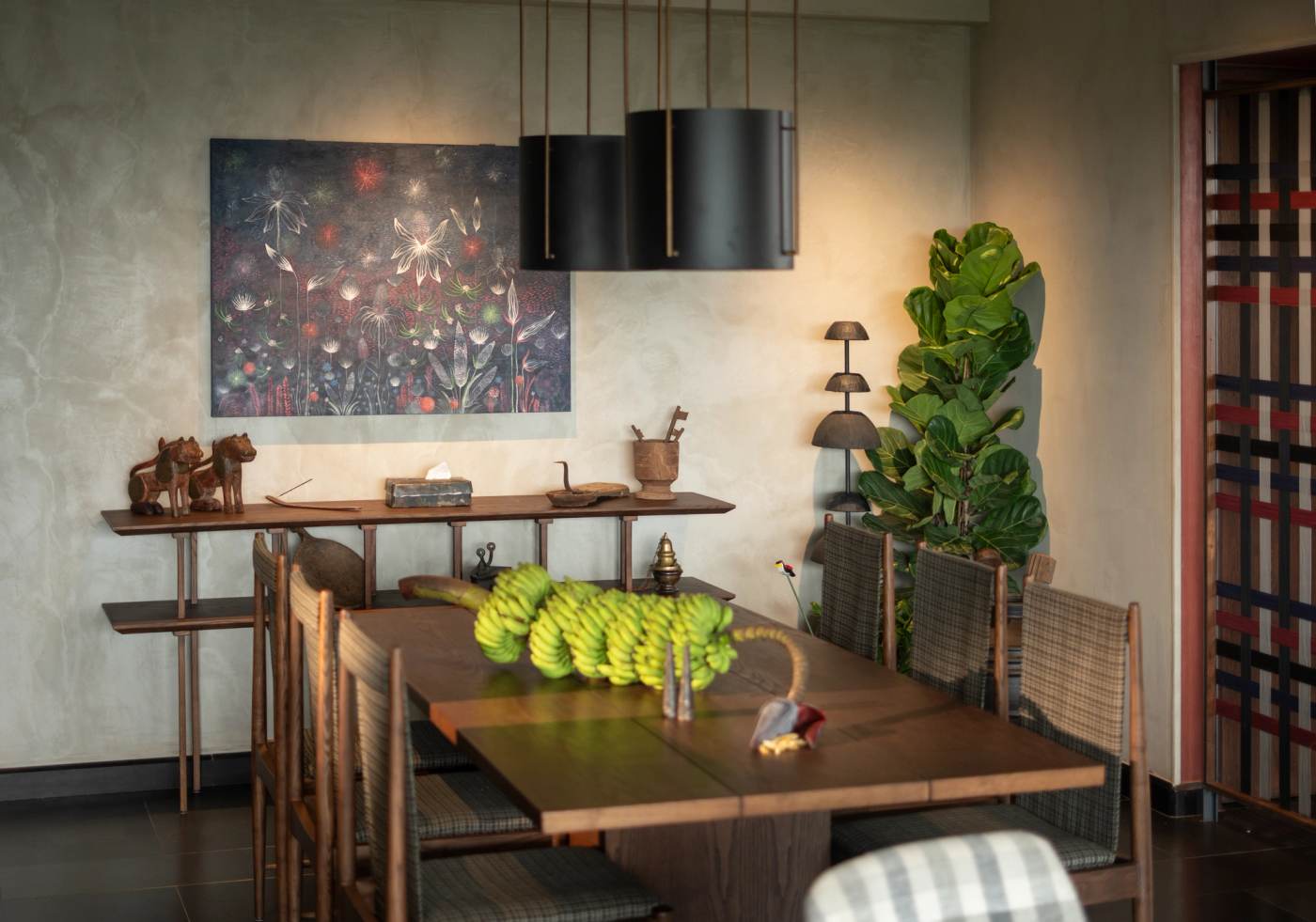 The dining table beneath a pair of black pendants, against a painting of white flowers