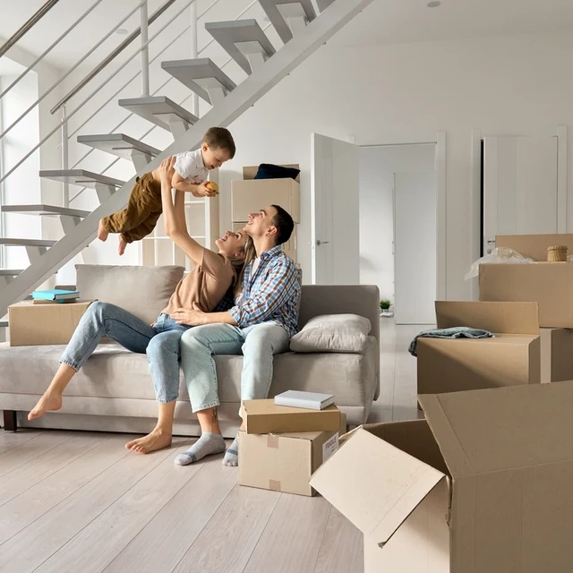 A happy couple holding a key to their new home, with moving boxes and a bright living space in the background.