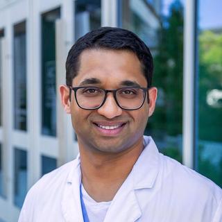 a man in a white lab coat and glasses is standing in front of a building .