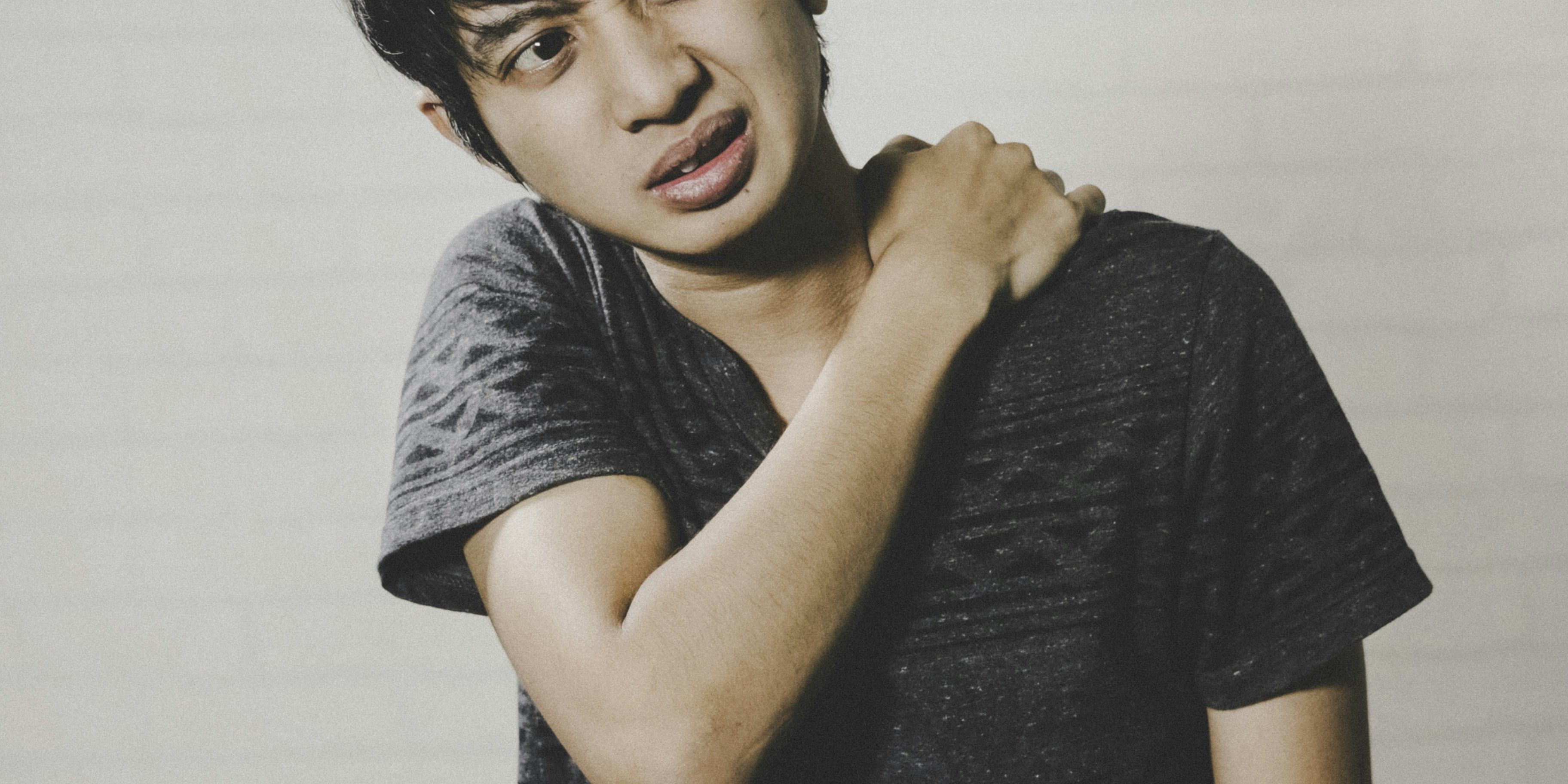 man holding his left shoulder and wincing in pain