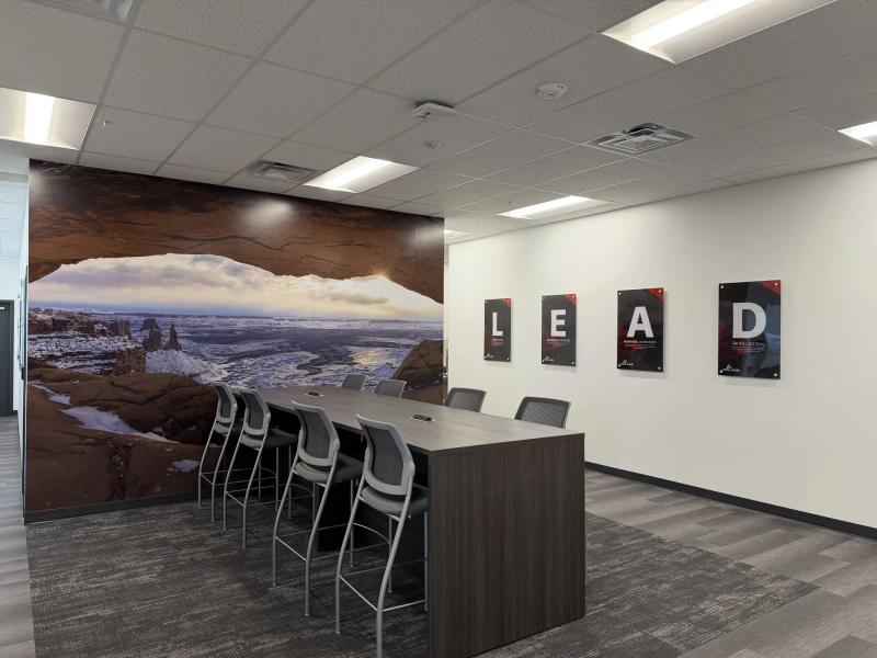 Full-wall printed mural of Mesa Arch at sunrise beside four standoff-mounted acrylic LEAD value panels in a McLane office break area