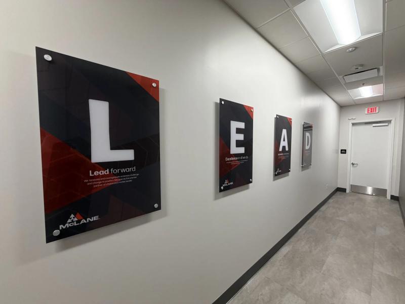 Hallway view of four printed acrylic LEAD panels mounted on brushed standoffs along a McLane office corridor