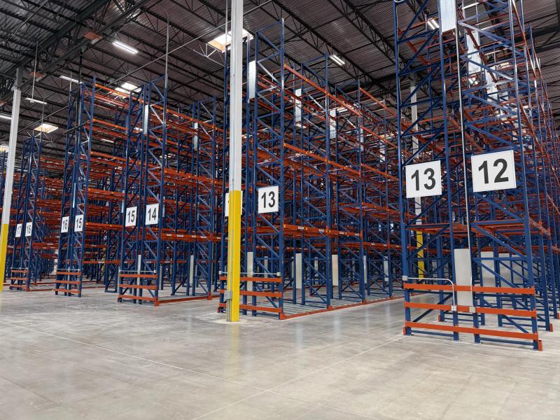 Rows of tall blue and orange pallet racking in a distribution center with large printed aisle number signs mounted on each end