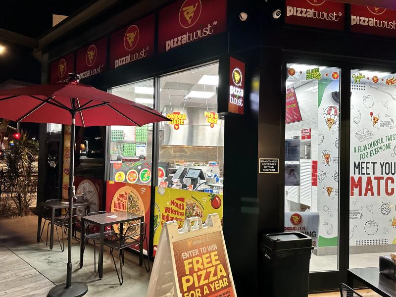 Pizza House storefront with printed window graphics, cabinet sign and promo A-frame at night