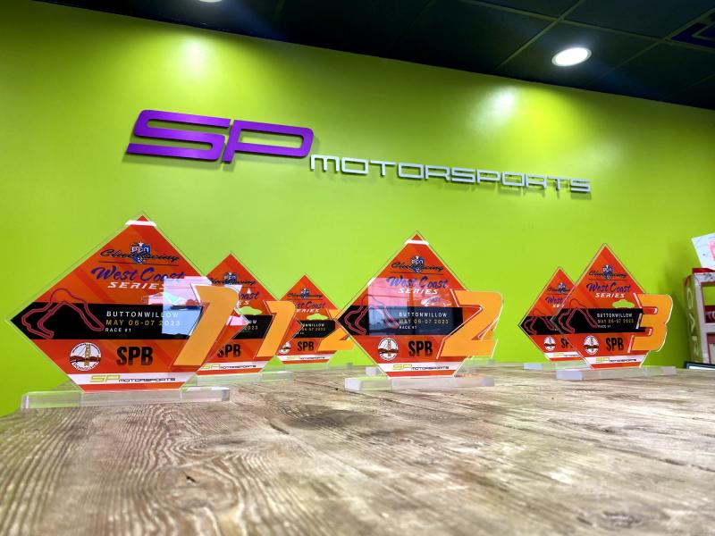 Display of custom printed acrylic awards for SP Motorsports against a lime-green feature wall