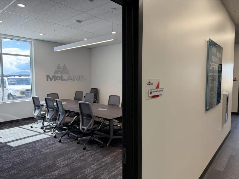 Conference room door with a branded room ID sign, a printed acrylic leadership panel, and brushed dimensional McLane letters on the far wall
