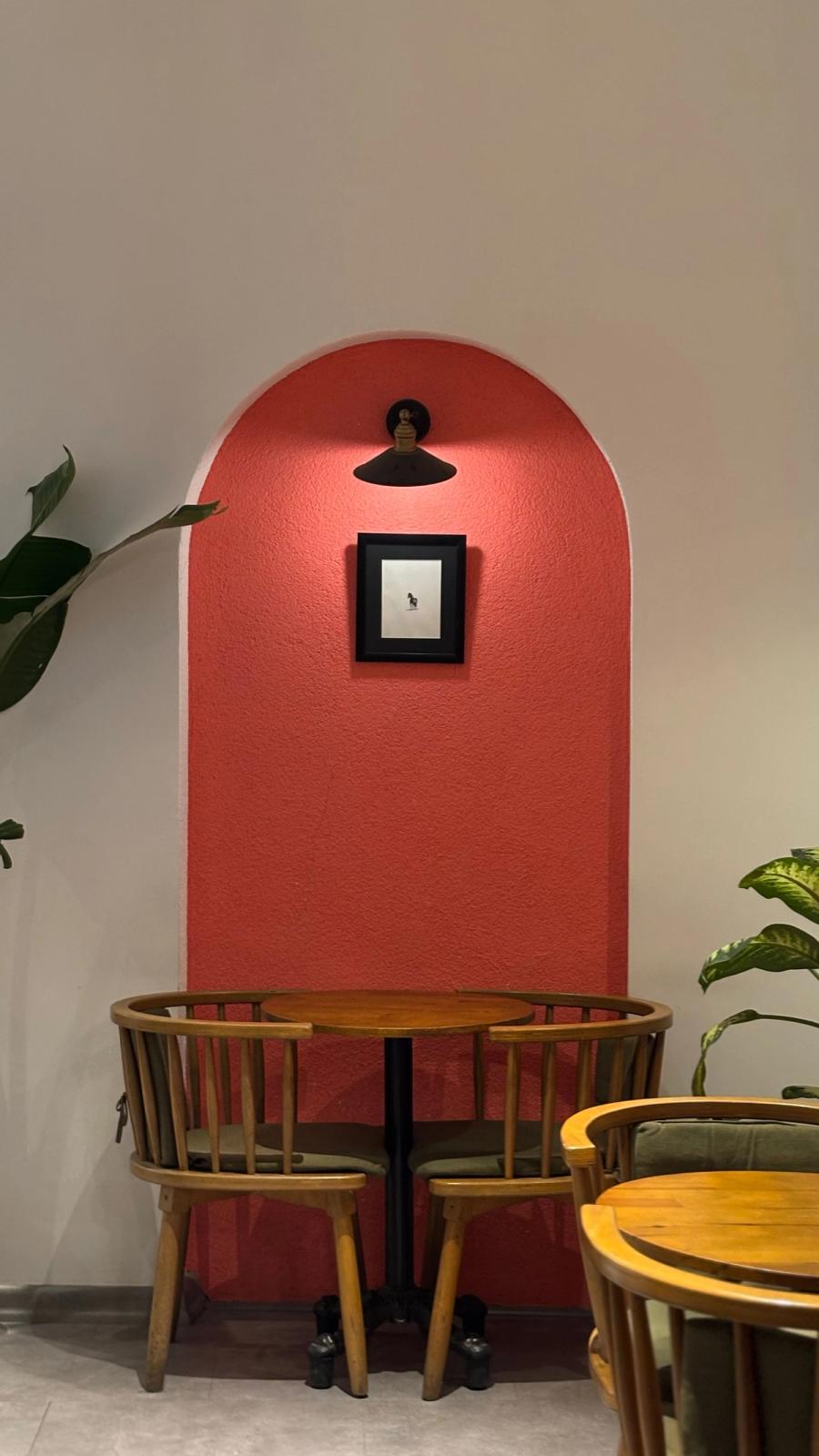 Arco pintado en color rojo coral en la pared con mesa y sillas de madera para decoración en Madrid.