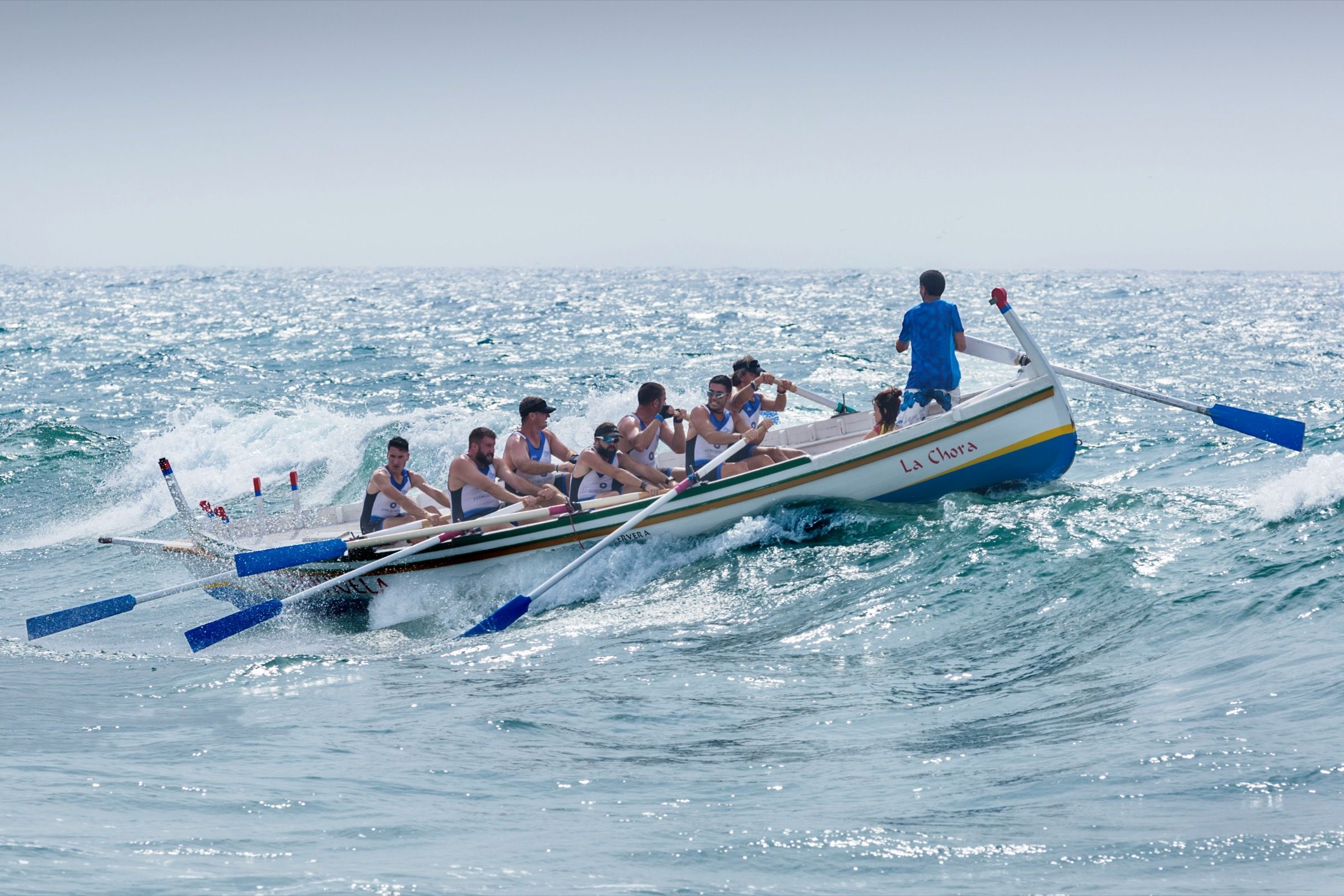 Ruderteam mit stehendem Steuermann in einem Holzboot auf bewegter See als Sinnbild für das Thema B2B-Software-Vertrieb skalieren