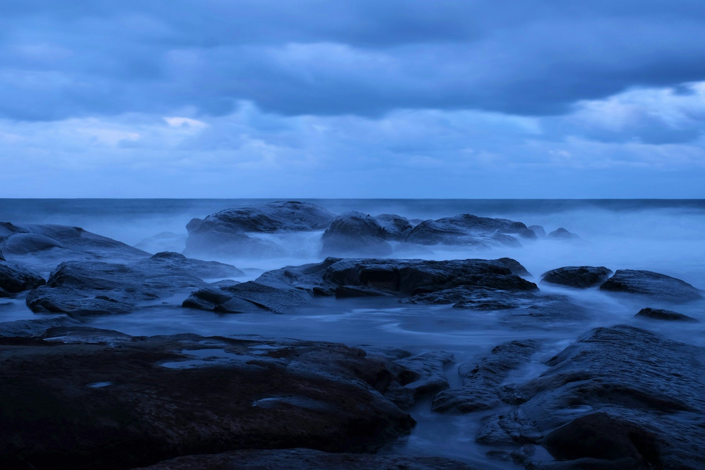Long-exposure surf around dark rocks at blue hour, symbolizing fast and slow change in the AI scenarios to 2029