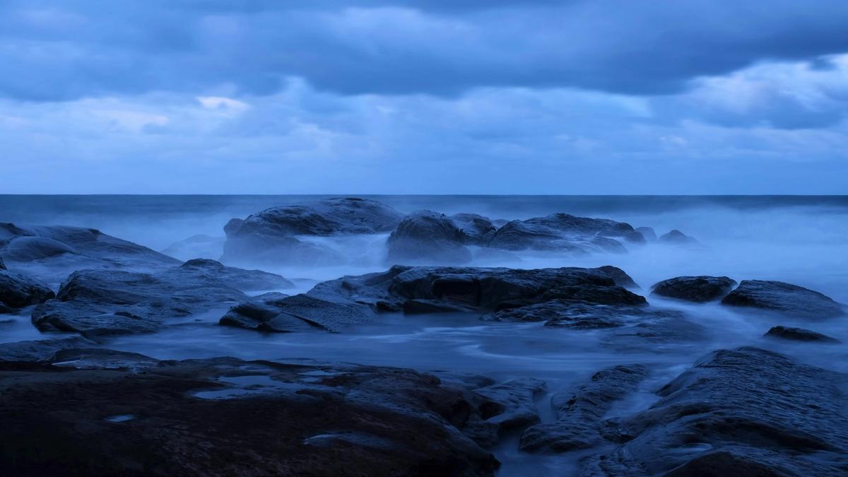 Long-exposure surf around dark rocks at blue hour, symbolizing fast and slow change in the AI scenarios to 2029