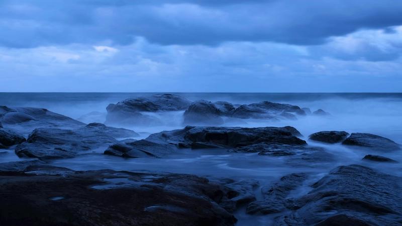 Langzeitbelichtete Brandung zwischen dunklen Felsen zur blauen Stunde als Sinnbild für schnellen und langsamen Wandel in der Zukunft der KI