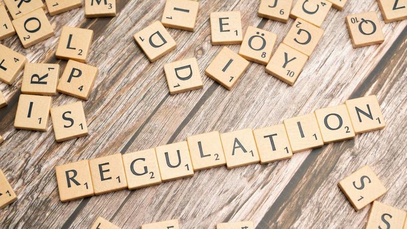 Buchstaben-Spielsteine bilden das Wort Regulation auf Holzuntergrund, KI-Regulierung Mittelstand 2026